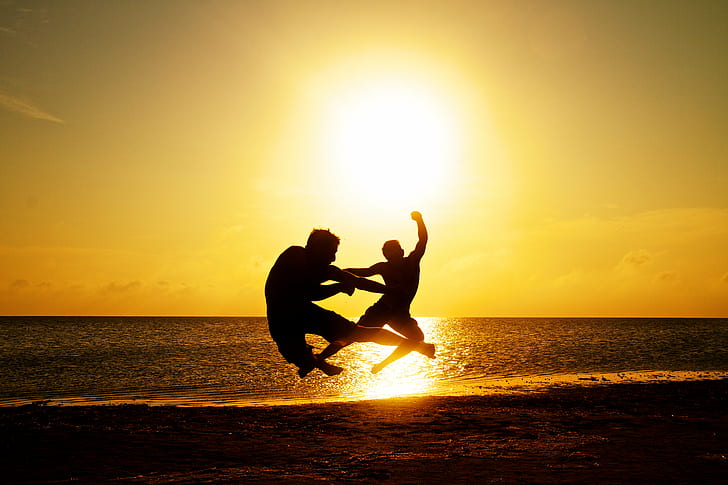 silhouette photo of two men jumping in seashore during golden hour