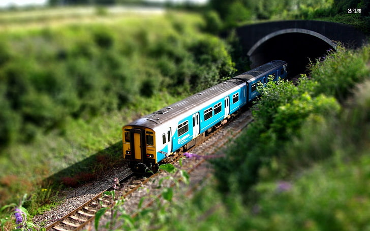 blue and beige train scale model, teal and white train surrounded by trees