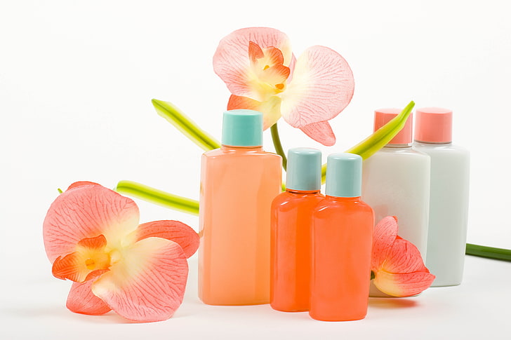 five assorted-labeled bottles, cosmetics, flowers, white background