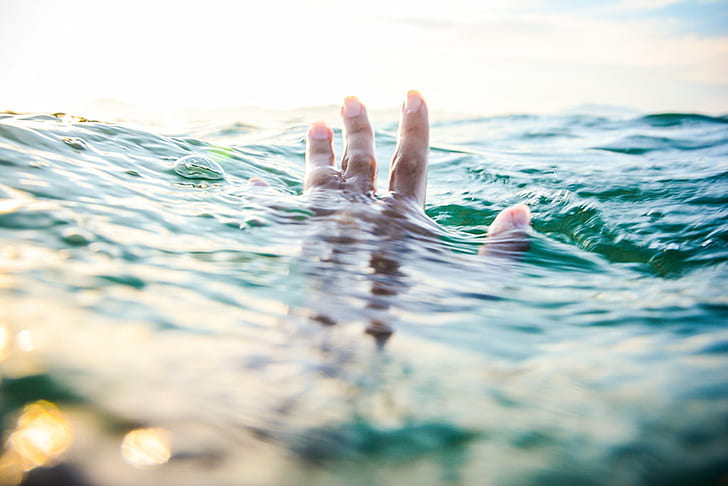 tilt shift lens photography of persons hand above body of water and his body under the water