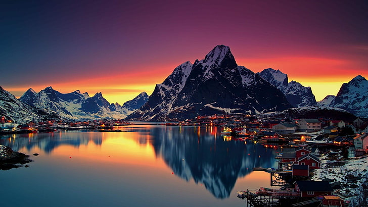town structures and body of water, clear calm body of water in front ice covered mountains under orange and blue sky