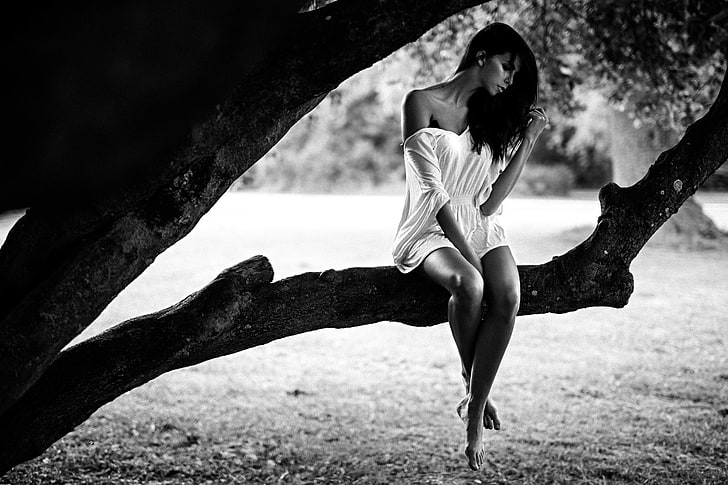 grayscale photo of woman wearing white dress sitting on tree trunk