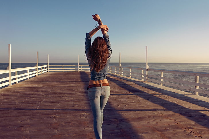 women's blue washed denim fitted jeans, woman walking on a dock raising her hands