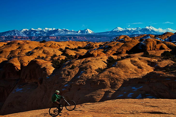 person riding bicycle on brown land within mountain range during daytime, HD wallpaper