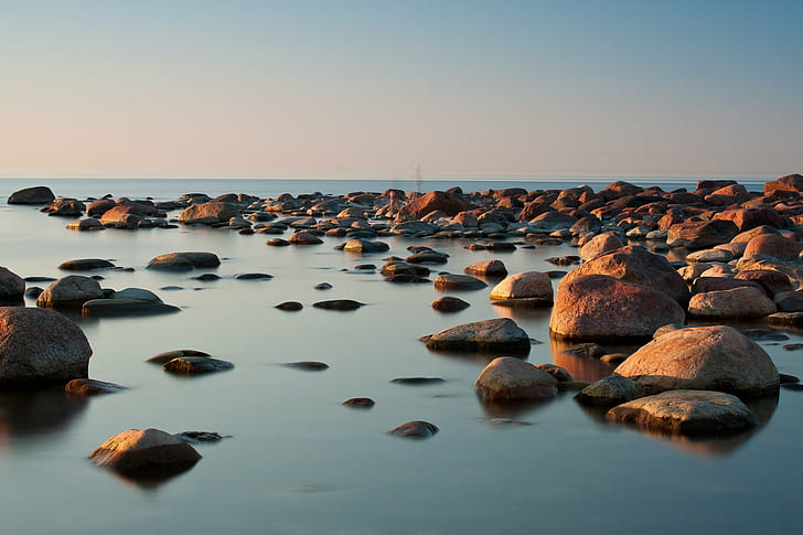 rocks on body of water under blue sky, shoreline, rocky, long exposure