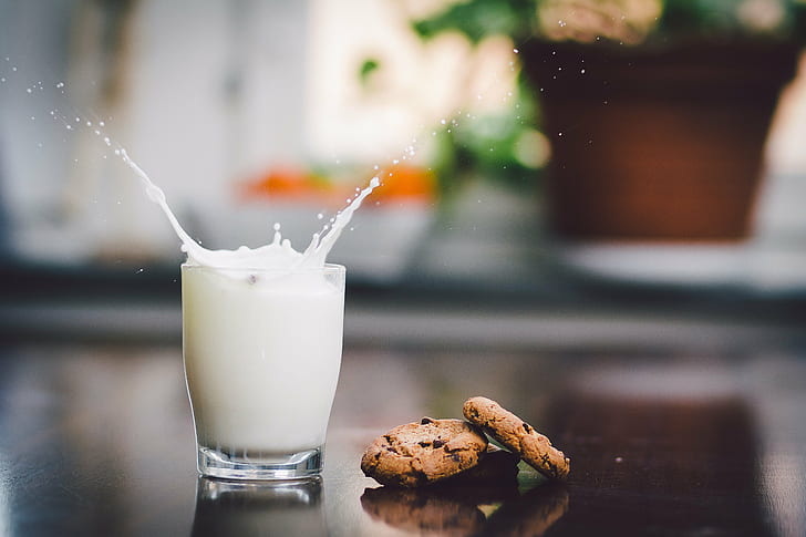 two chocolate dip cookies beside glass of milk, splash, bokeh