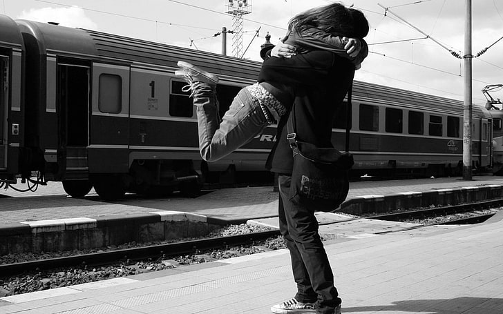 grayscale photo of couple hugging in front of train, monochrome