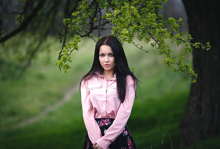 women's pink denim jacket, woman in pink dress shirt and black and pink floral skirt standing below tree branch