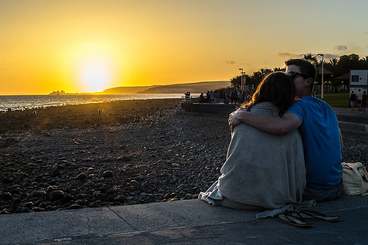 couple holding each other sitting near beach during golden hour