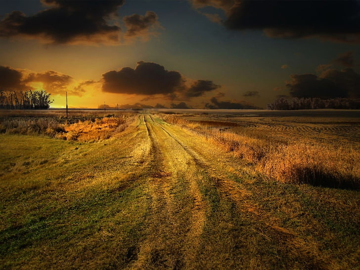 green grass field and pathway under blue and orange sunset sky