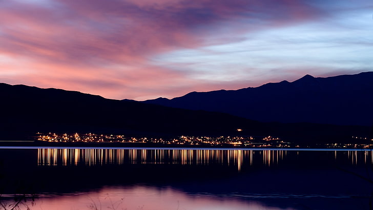 body of water, reflection of city lights on body of water on mountain slope during sunset