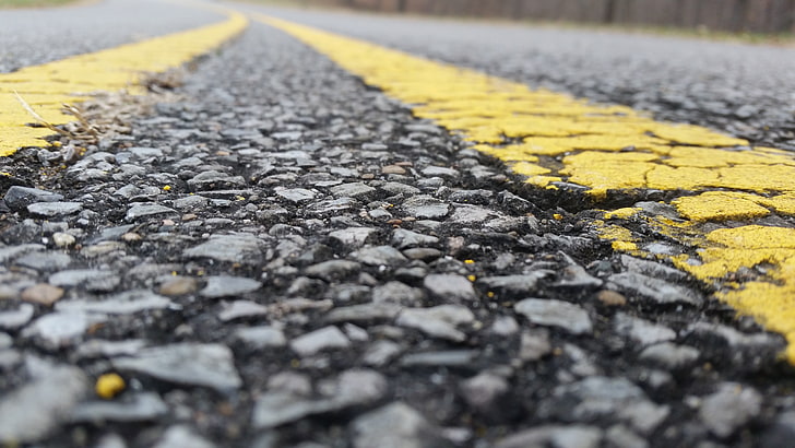 closeup photo of black top road with yellow paint lines, no people