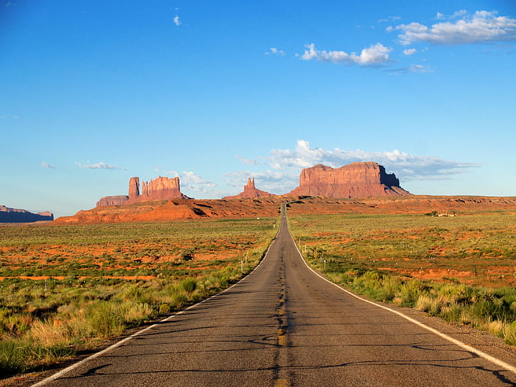 asphalt road in middle of grass field under blue sky, monument Valley