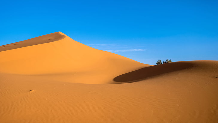 A large sand dune with a blue sky in the background photo – Free