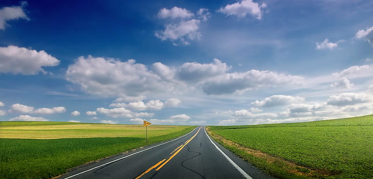 empty road between green grass under white and blue cloudy sky