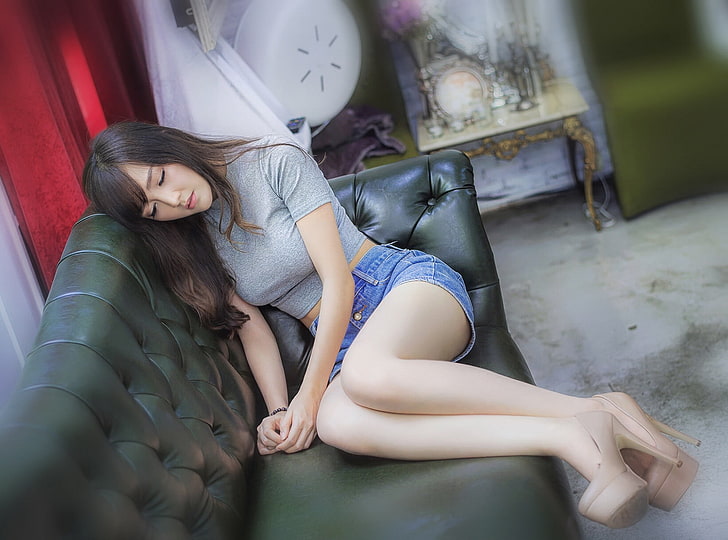 woman wearing gray crop top and blue denim short shorts sitting on black leather sofa