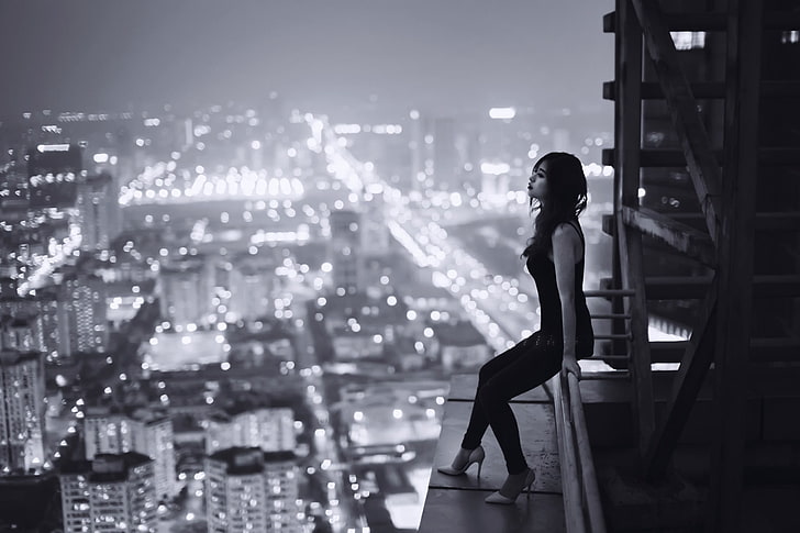 grayscale photo of woman sitting on pole on top of building, grayscale photo of woman sitting on building