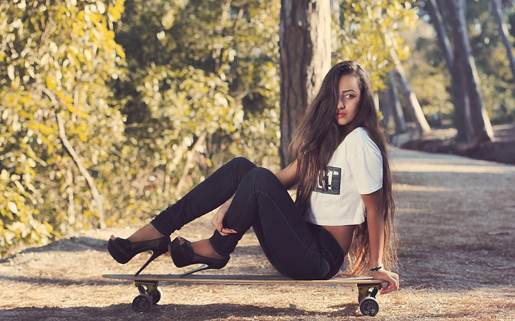 woman in white crop t-shirt and black pants sitting on brown longboard beside tree during daytime