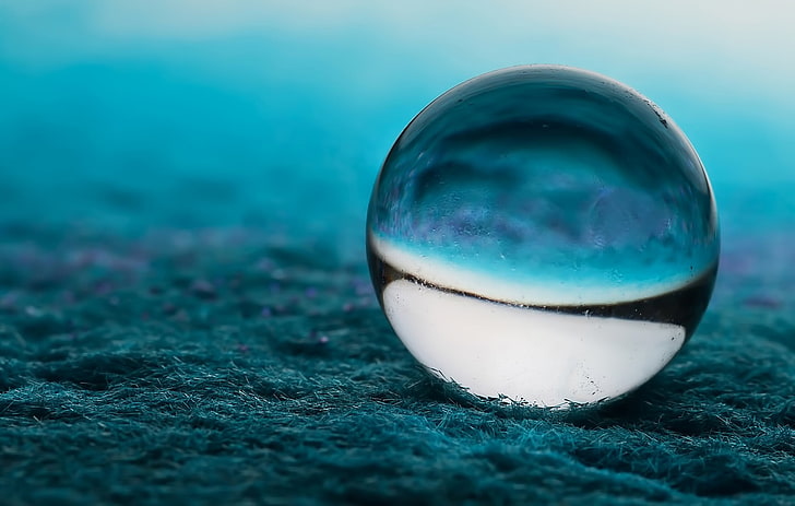 white and blue marble toy, clear glass ball on top of blue soil