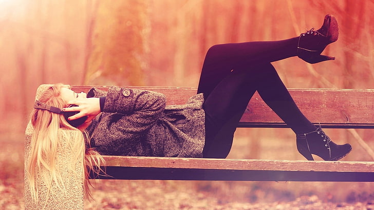 woman lying on brown bench holding headphones, blonde, music