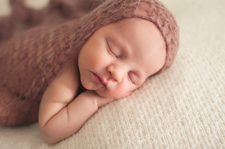 baby in brown knitted textile sleeping laying on white textile