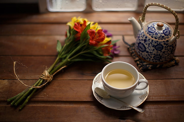 photography of white ceramic teacup set; blue and white ceramic teapot; and red and yellow petaled flowers